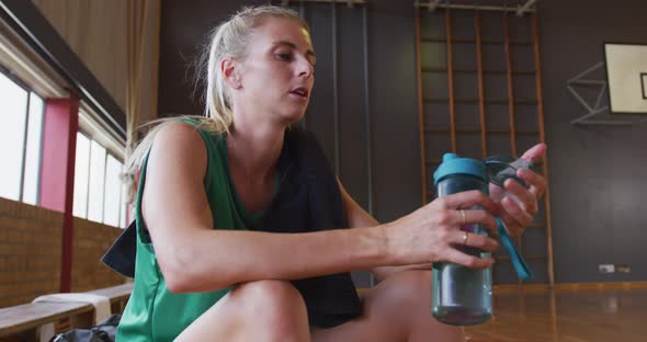 Caucasian female basketball player resting and drinking water
