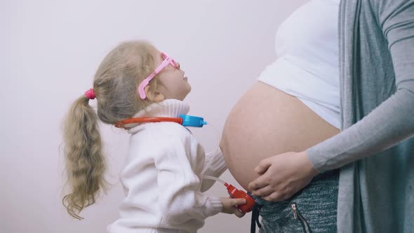 Child with Toy Stethoscope Listens To Pregnant Mummy in Room