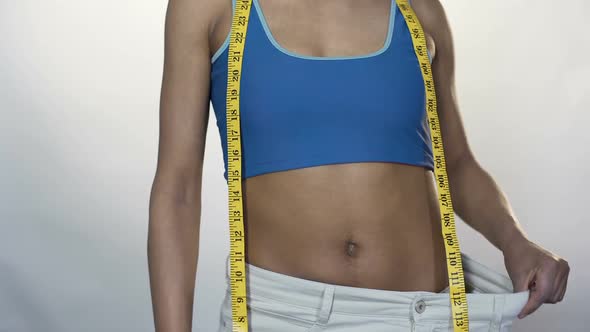 Fit Woman Pulling Waist of Oversized Pants Away, Showing Thumbs-Up, Weight Loss