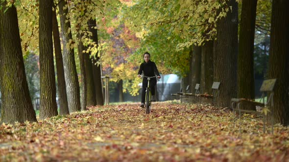 Young Woman Rides Bike Toward Camera at City Park in Autumn Fall Season