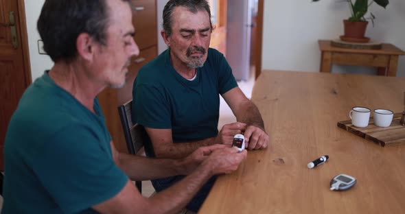 Senior men checking blood sugar level to his twin brother at home