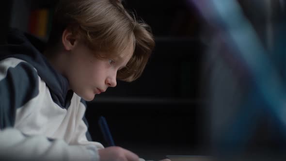 Side View of Focused Child Little Boy Kid Writing to Notebook with Pen Looking on Paper Book