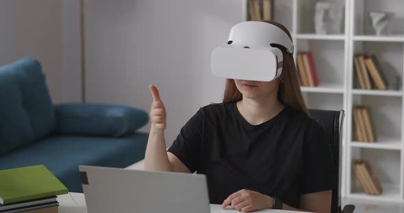 Woman Is Wearing Headmounted Display for Viewing Virtual Reality Sitting at Home Gesticulating By