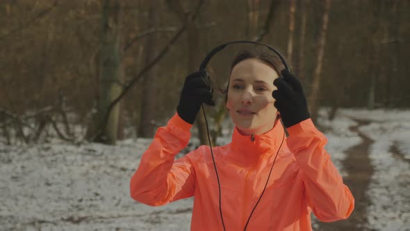 Cute smiling female puts on headphones in park before run. Running concept