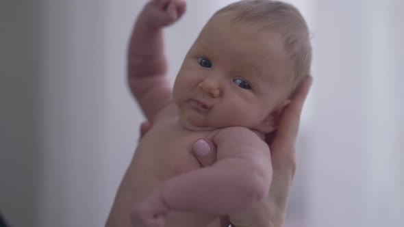 Small Naked Newborn Baby Girl in Female Hand Looking at Camera