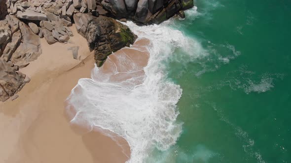 Birdseye View of Waves Crashing onto Shore Alongside Rocks