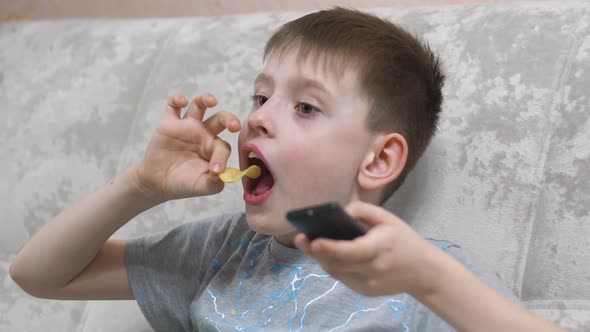 Portrait of a caucasian boy 7-8 years old with an open mouth watching TV with surprise, holding a re