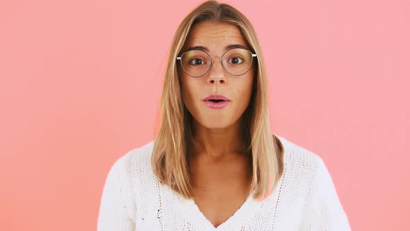 Young Lady in Glasses and White Jumper is Looking Surprised Saying Wow and Smiling While Posing on