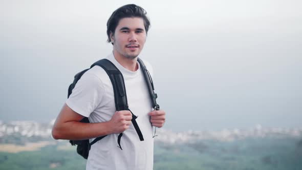 Adventure Trip Young Man Hiker Stands on the Top on a Mountain and Looking in the Camera Waving with