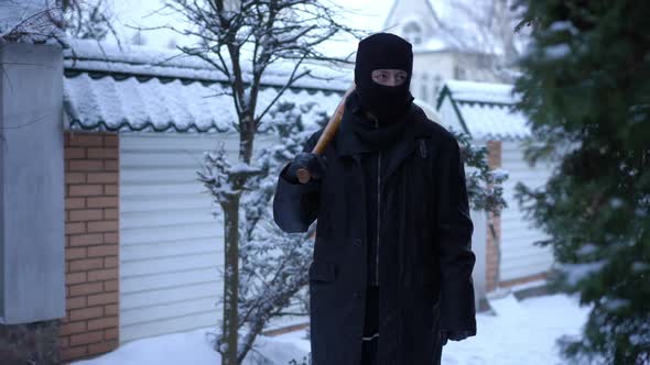 Dolly Shot of Caucasian Male Robber Walking with Baseball Bat on Snowy Winter Backyard