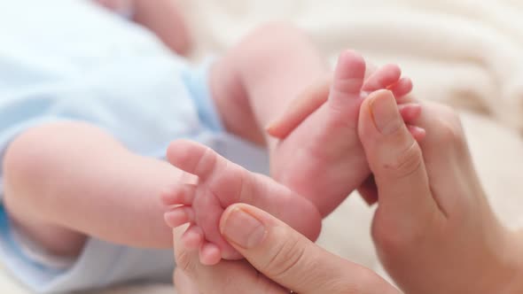 Closeup of Young Caring and Loving Mother Massaging and Stroking Little Feet of Her Newborn Baby Son