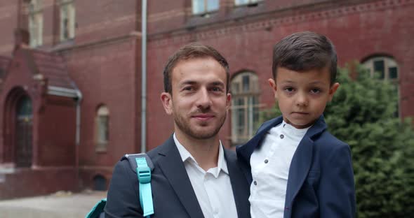 Close Up View of Happy Dad and His Cute Son Looking To Camera and Smiling. Young Man in Suit Holding