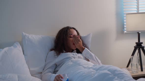 Latino beautiful sick woman in pajamas taking medicine before sleep.