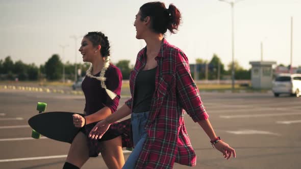 Side View of Two Young Happy Hipster Girls Walking Together in the Parking Talking and Laughing