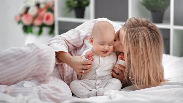 Joyful Mother Kiss Little Toddler Lying Together on Comfortable White Blanket