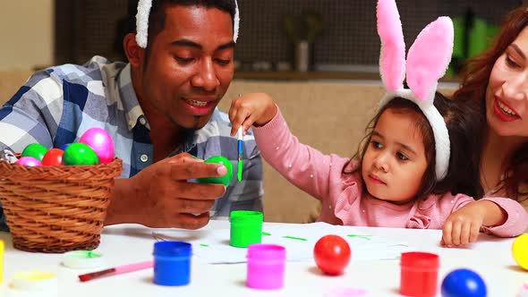 Multicultural Cute Little Child Girl Wearing Bunny Ears on Easter Day Painting Egg in Kitchen with