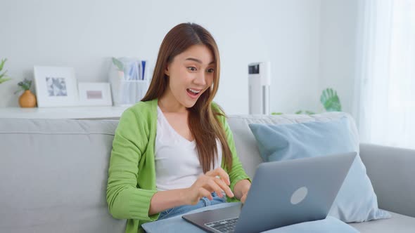 Asian young business woman typing on computer and working from home in living room.