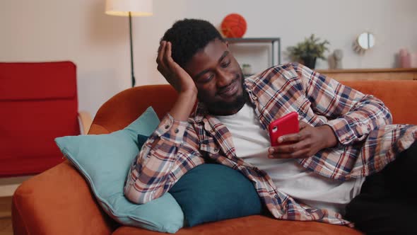 Cheerful Young Man Lying on Sofa Using Mobile Phone Share Messages on Social Media Application