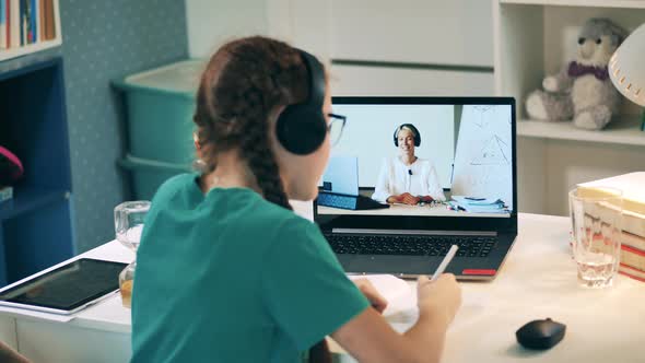 Girl Waving at the Camera While Talking To a Teacher During an Online Class