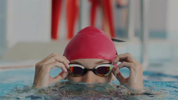 Closeup Portrait. Young Female Athlete in Red Swim Cap Appear From the Water in the Swimming Pool