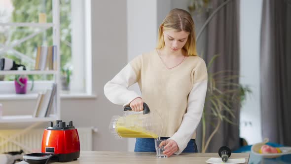 Middle Shot of Slim Gorgeous Young Woman Pouring Fruit Smoothie in Glass and Drinking Healthful