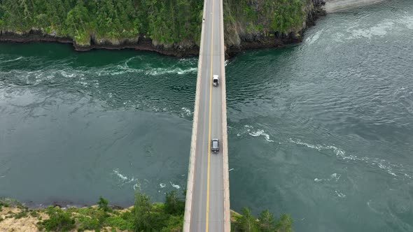 Overhead aerial view of cars driving along the Deception Pass bridge over the Pacific Ocean.