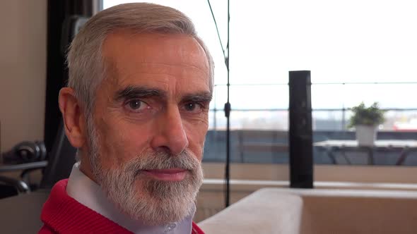 A Happy Elderly Man Sits on a Couch in an Apartment and Smiles at the Camera