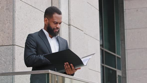Serious Focused African American Businessman Analyst Standing on Balcony Holding Sheets Check