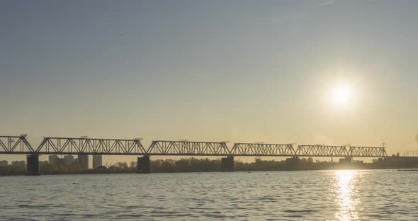 Timelapse of City River Bank. Sun Rays, Blue Sky and Railway Bridge Over Horizont. Summer Sunset