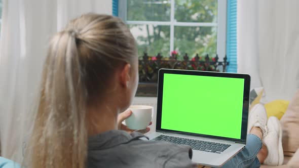 Young Woman Relaxing on Sofa with Cup of Tea and Laptop