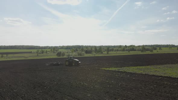 Agricultural green big tractor plows in the field.