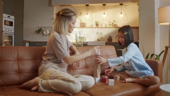 Happy Asian Young Mother and Little Daughter Sitting at Sofa and Playing Together