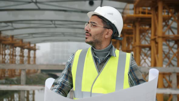 Serious Arab Guy Engineer Checking Construction Plan and Looking Around Outdoors