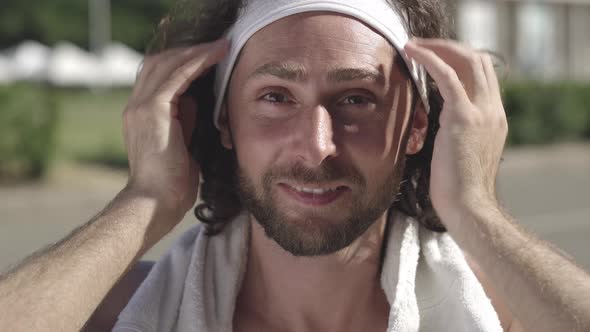 Close-up Face of Happy Handsome Caucasian Bearded Man with Brown Eyes Adjusting Headband and Smiling