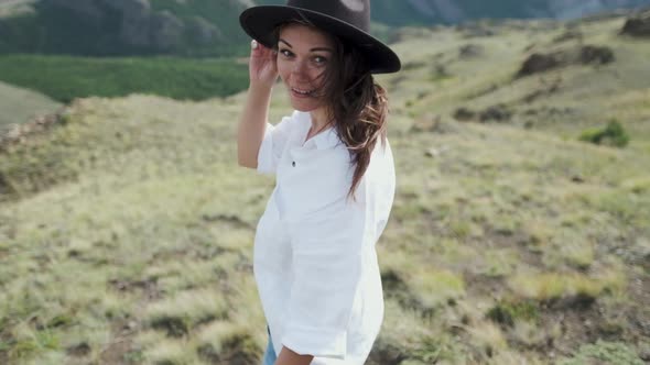 Attractive Brunette in a Hat and White Shirt Is Enjoying Nature in the Mountains. Beautiful Young