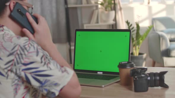 Man Editor Talking On Mobile Phone And Works On His Laptop Computer With Green Screen Display