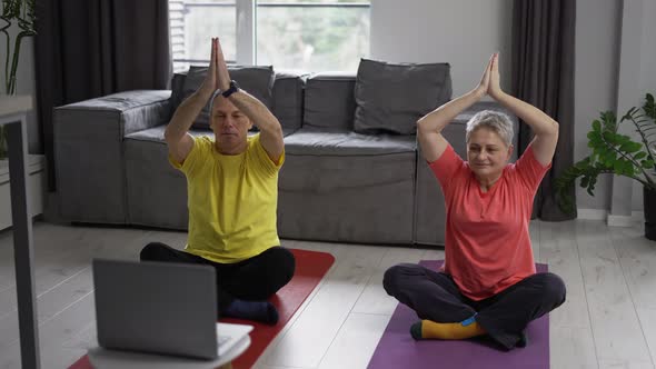 Active Mature Couple Performing Stretching Exercise By Online Workout Lessons Using Laptop