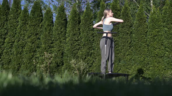 girl does Jumping fitness on trampoline in outdoor on green grass and trees on background