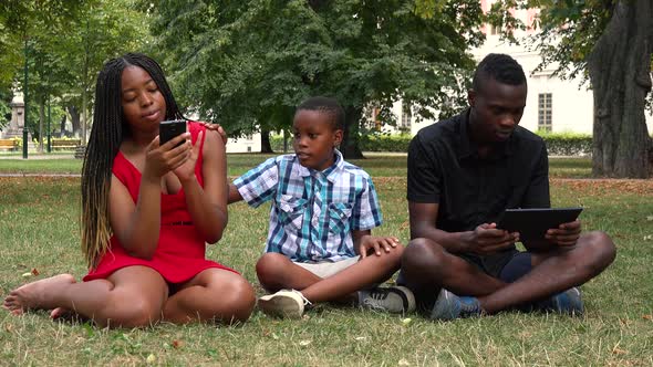 A Black Boy Tries To Attract Attention of His Parents Who Are Absorbed in a Smartphone and a Tablet