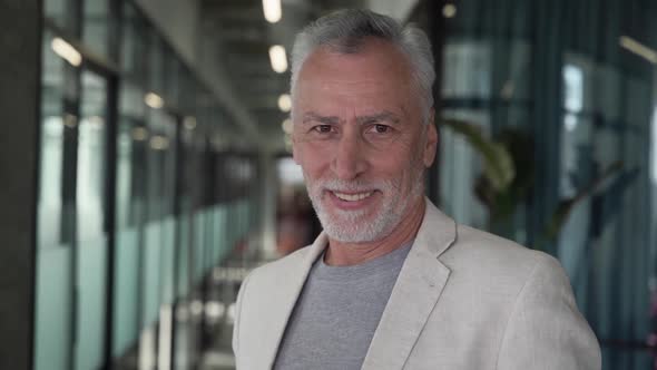 Happy handsome grey haired businessman taking off his glasses, while posing in co-working interior