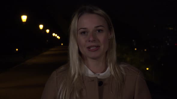 A Young Beautiful Woman Talks To the Camera with a Smile in an Urban Area at Night