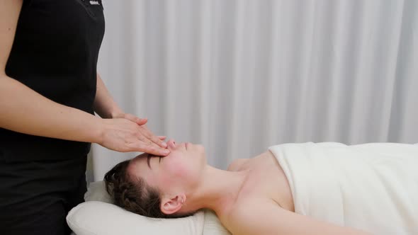 Female therapist massages the head and face of a young woman. Relaxing massage. Therapeutic massage.