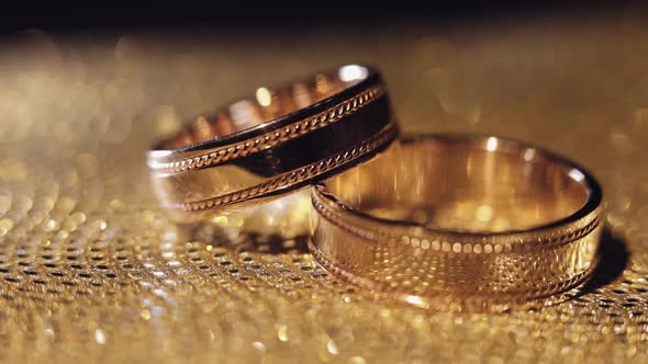 Wedding Rings Lying Rotate Spinning on Shiny Golden Shining Surface with Light Closeup Macro