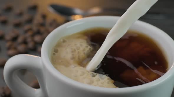 Close up slow motion shot of an artisan barista pouring milk into a hot cup of black coffee creating