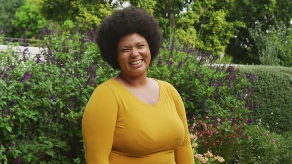 Video of happy plus size african american woman standing in garden