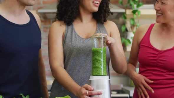 Group of diverse young people making green healthy smoothie together at home