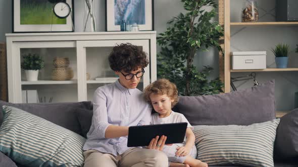 Mother and Son Using Tablet Looking at Screen and Talking on Sofa in Cozy House