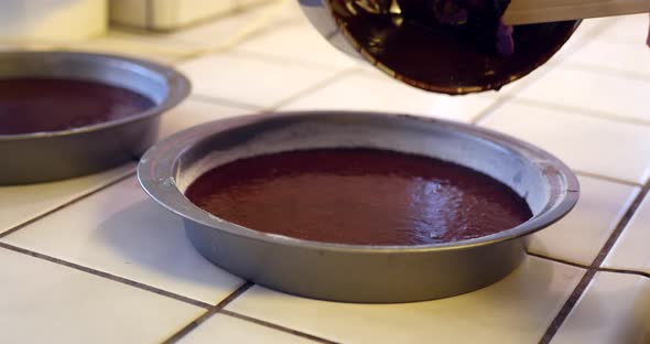 A chef in the kitchen pouring and scooping delicious vegan chocolate cake batter into a round baking