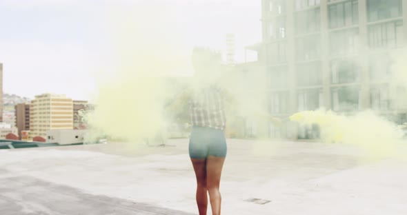 Fashionable young woman on urban rooftop using smoke grenades