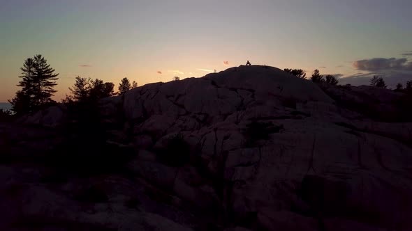 Inukshuk on Rocky Pine Tree Island at Sunset, Drone Aerial Wide Pedestal Up. Reveal of Blue Lake, Co